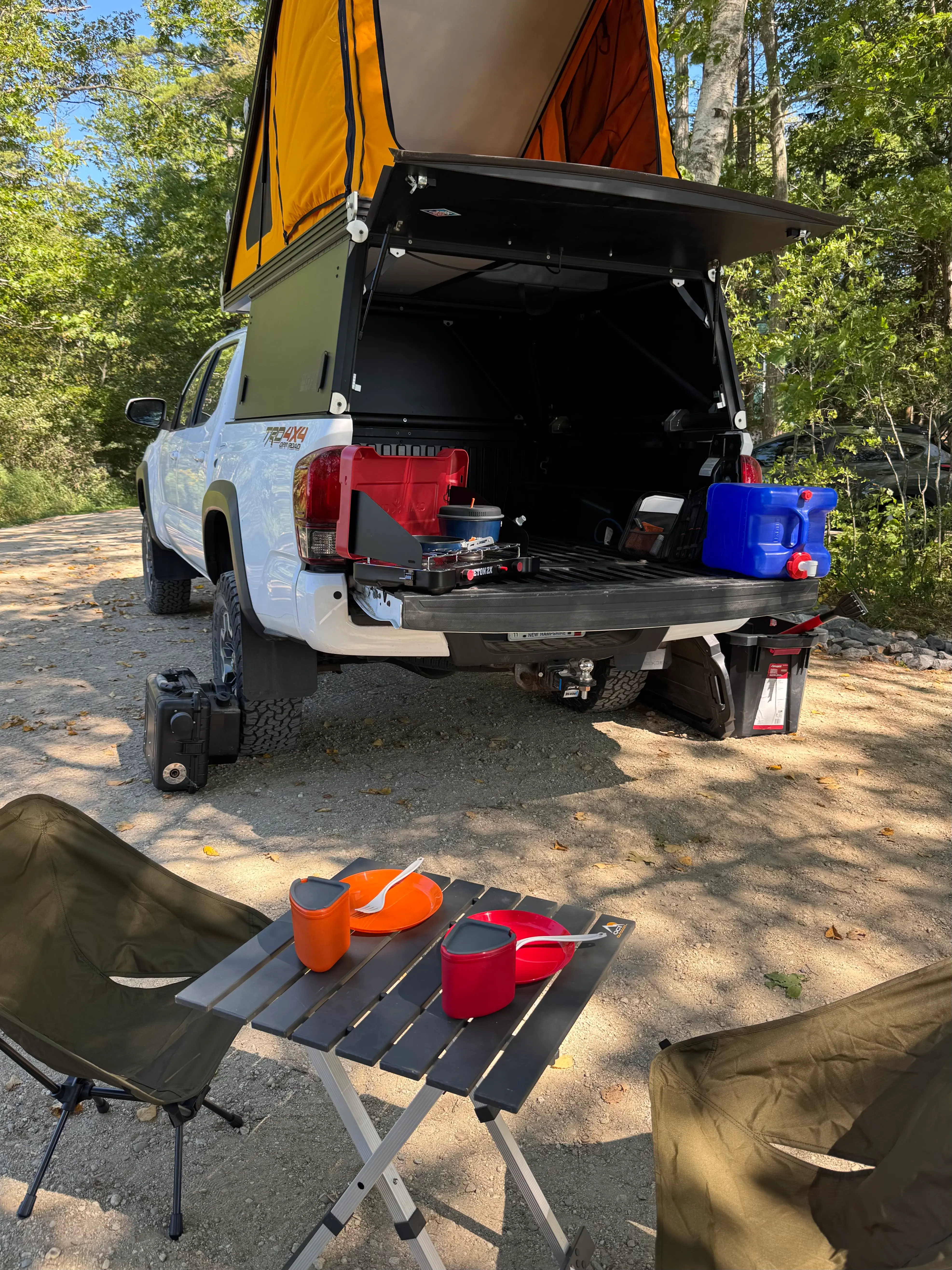 Tailgate camp kitchen with a two-burner stove and cookset set up at a forest campsite