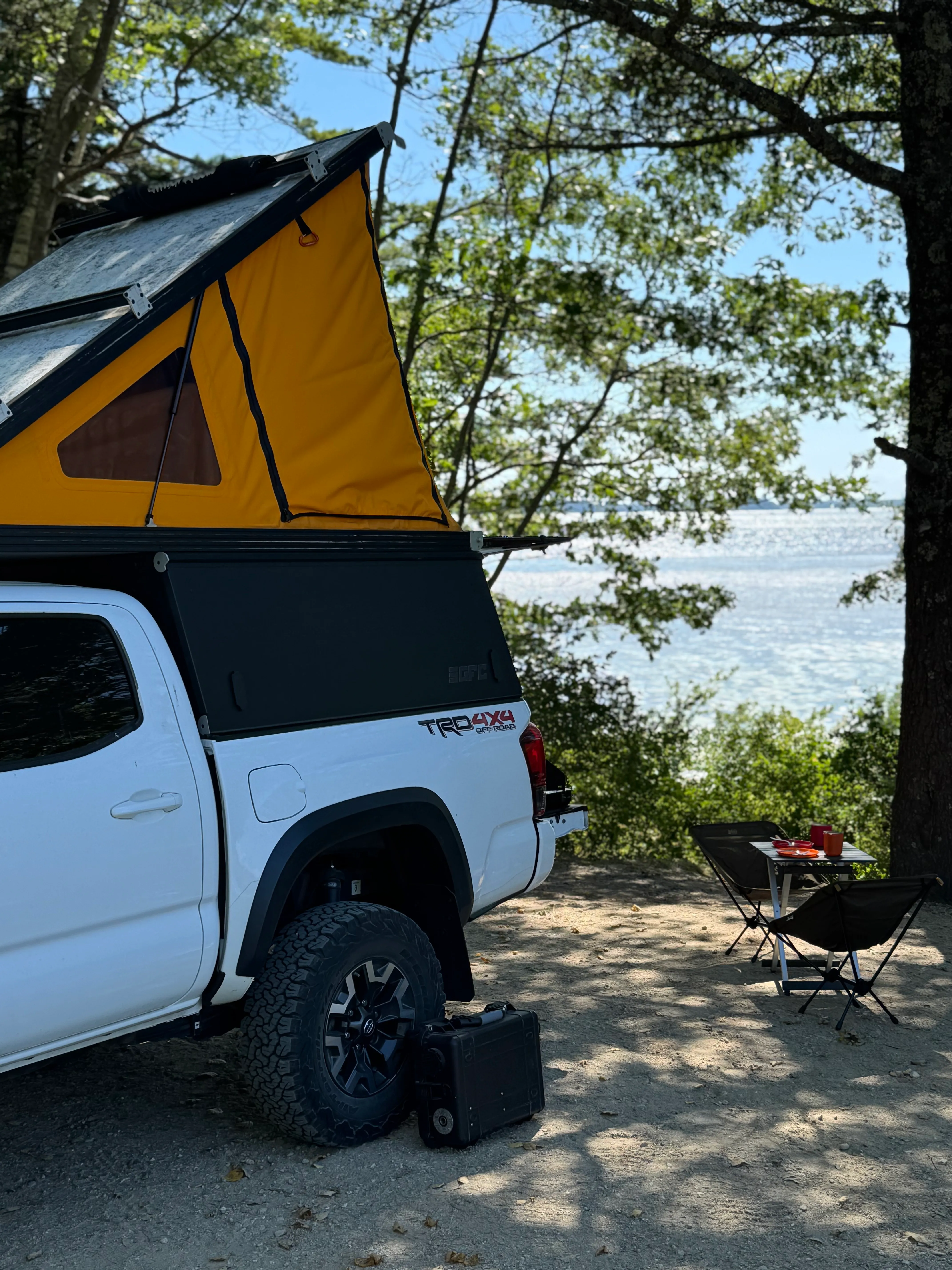 The Toyota Tacoma TRD with its Go Fast Camper open at a New England coastal campsite, camp chairs and table set up by the water