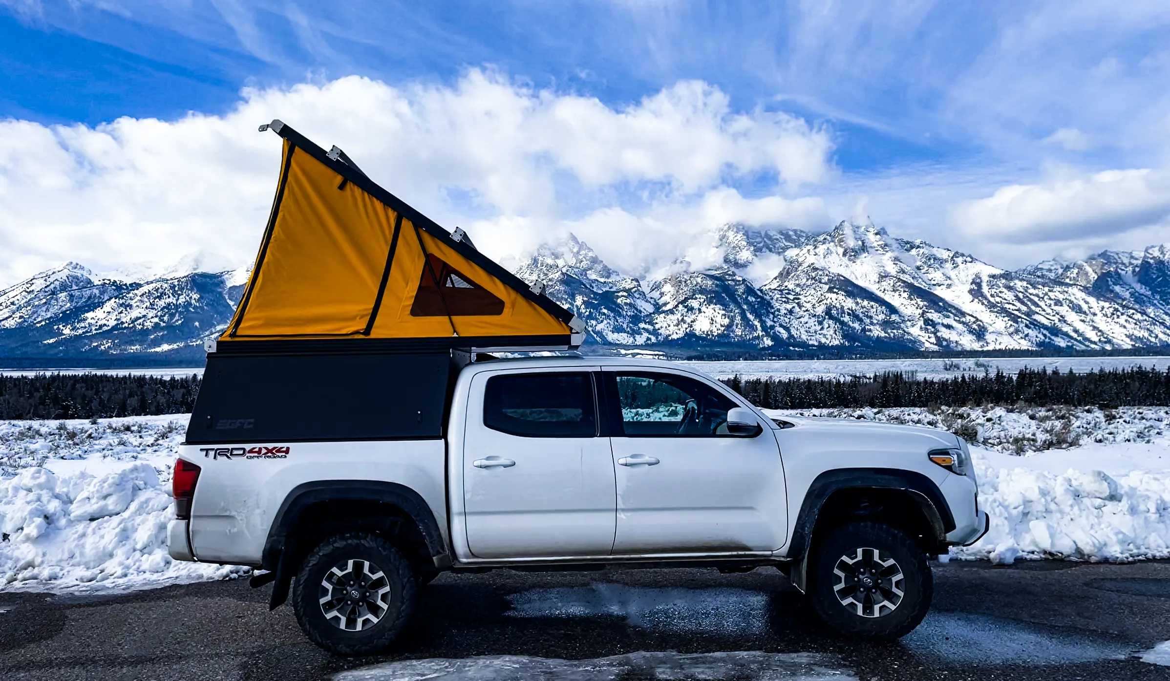 Toyota Tacoma TRD Off-Road with a Go Fast Camper pop-up camper open, parked at a snowy mountain overlook